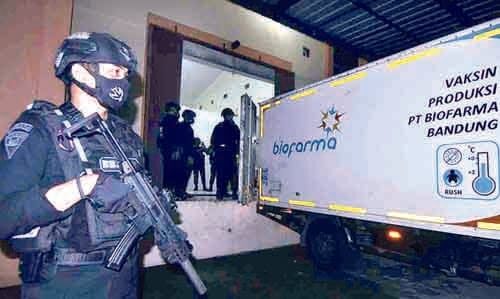 PENJAGAAN— Terlihat seorang anggota Brimob dengan senjata lengkap berjaga di samping truk berisi vaksin Covid-19.