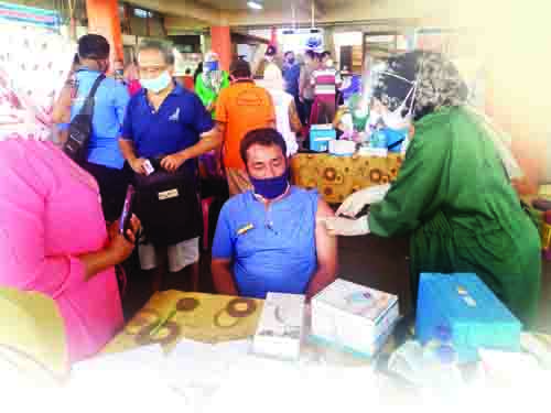 DISUNTIK VAKSIN— Koordinator retribusi harian Pasar Raya Padang, Usman Gumanti disuntik vaksin oleh petugas Dinkes Kota Padang, Kamis (4/3) di lobi Blok III Pasar Raya Padang.