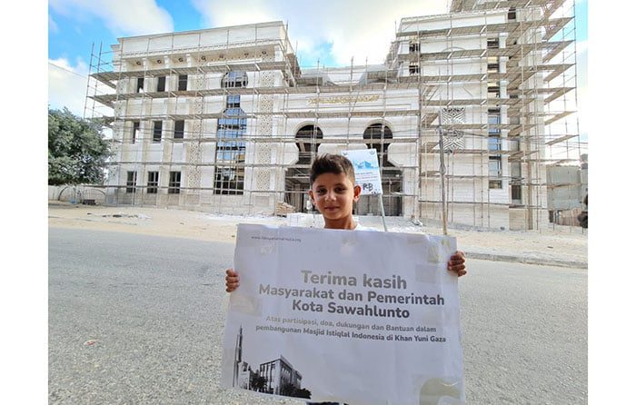TERIMA KASIH—Seorang anak Palestina di depan Masjid Istiqlal Indonesia di Palestina membentangkan spanduk ”Terima kasih untuk masyarakat dan Pemko Sawahlunto yang telah membantu kami membangun masjid”.