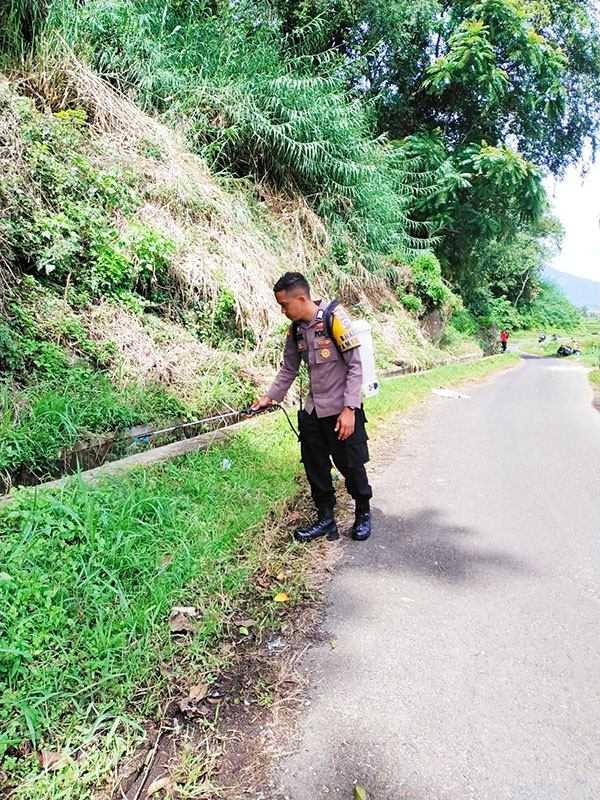 Bhabinkamtibmas Polsek X Koto, Polres Padangpanjang Bripka Alex Wijaya menyandang mesin pompa pembasmi rumput liar saat Goro bersama warga.