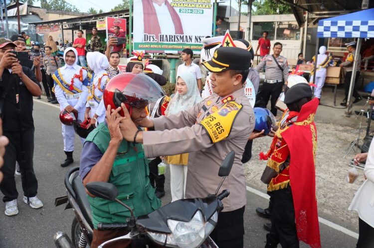 PASANGKAN HELM— Kapolres Pasbar AKBP Agung Tribawanto, memasangkan helm kepada salah seorang pengendara di bundaran Simpang Empat.