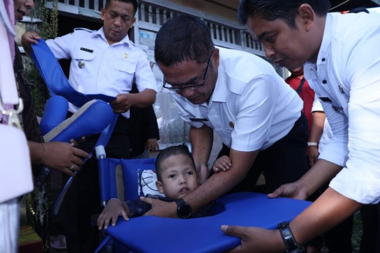 Pemko Berikan Kursi Roda Pada Anak Penderita Hidrosefalus 1 KURSI RODA DUA— Sekda Kota Payakumbuh Rida Ananda menggendong Ikhsan dan mencobakan kursi roda baru untuknya.
