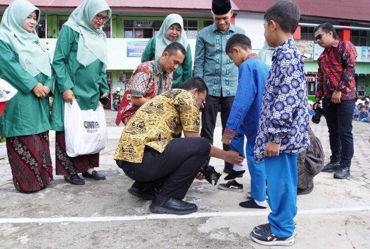 PAKAIKAN SERAGAM— Pj Wako Padang Panjang Sonny Budaya Putra, pakaikan sepatu dan seragam kepada seorang pelajar yang menerima bantuan seragam dan perlengkapan sekolah, Kamis (12/9).