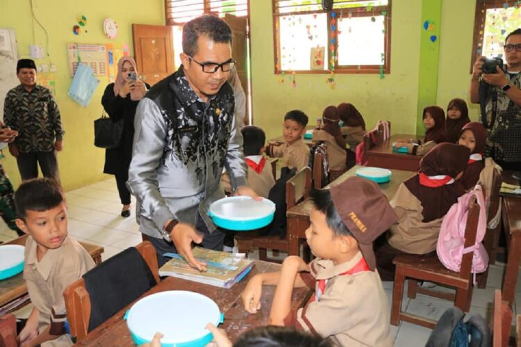 Pemberian MBG di Lingkungan Sekolah, Sempat Dihentikan, Sekarang Telah Dimulai Kembali 1 BAGIKAN—PLT Kpala Dinas Pendidikan Pemuda dan Olahraga (Dikpora) Kota Pariaman, Riky Falantino, saat bagikan MBG.